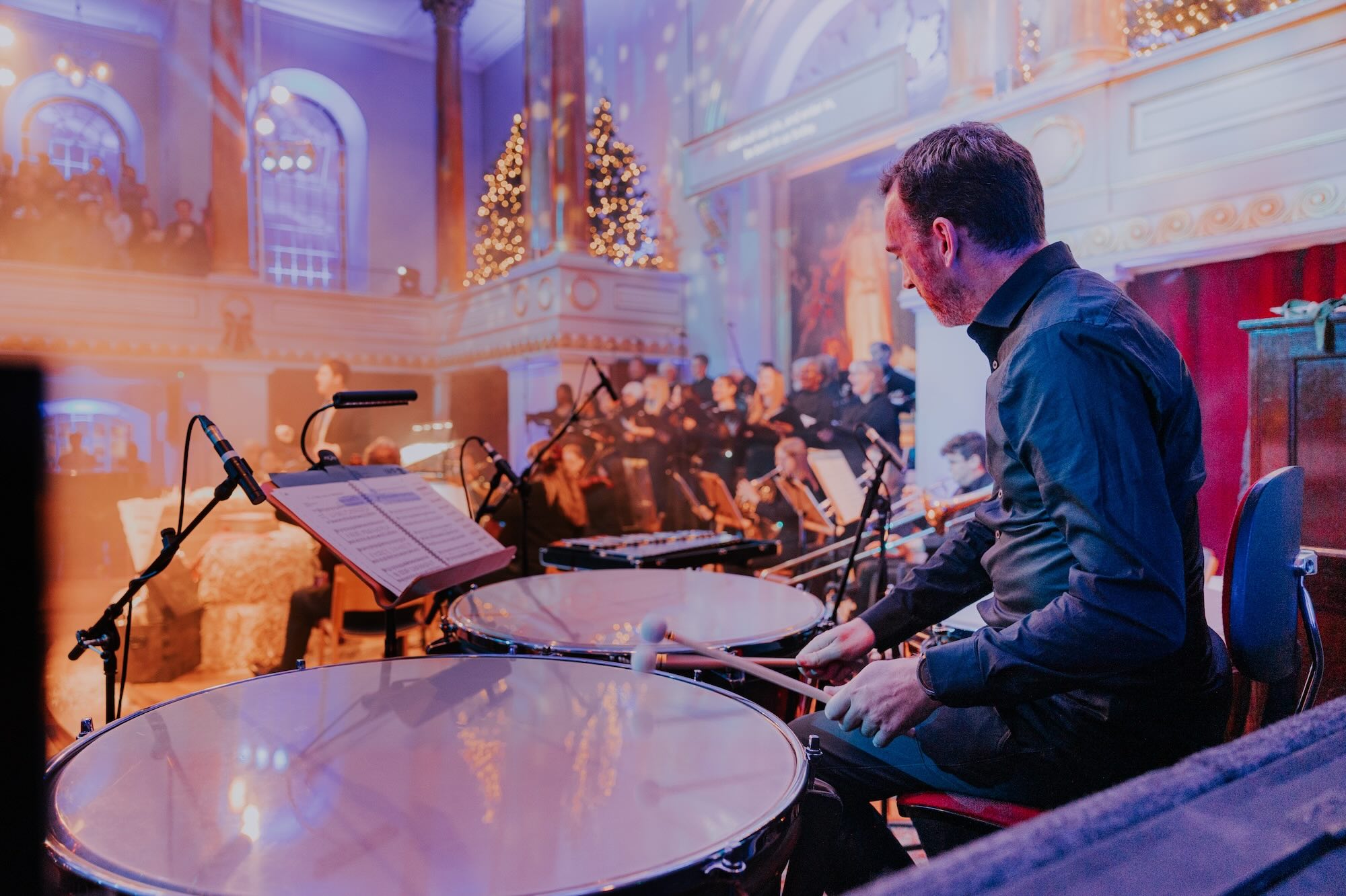 Musicians accompany a Christmas carol at the All Souls carol service, engulfed in a haze of festive lights.
