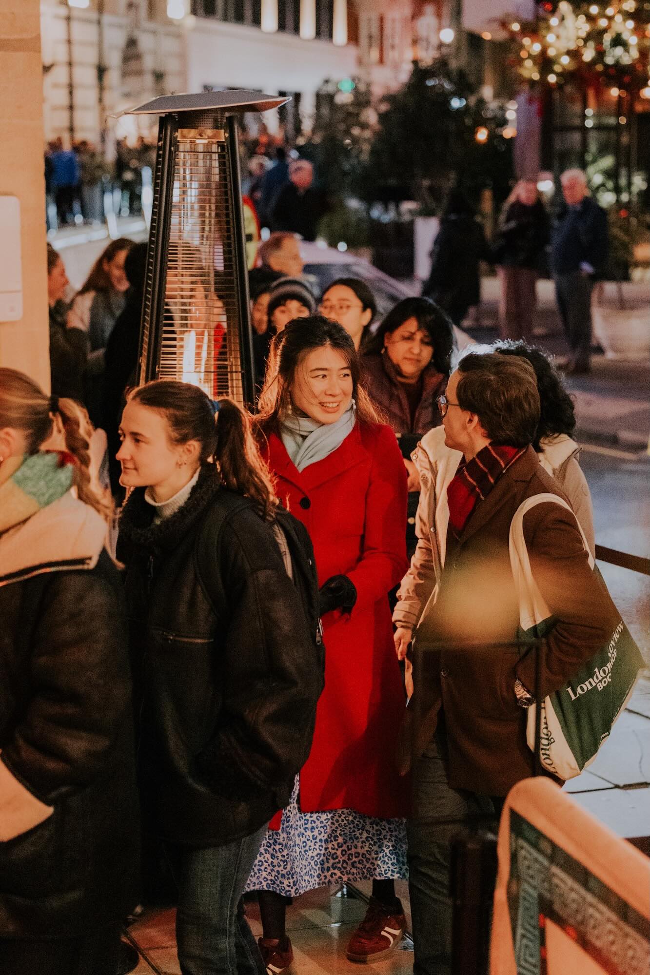 Festive visitors keep warm by the fire, as they wait to enter All Souls Carols.